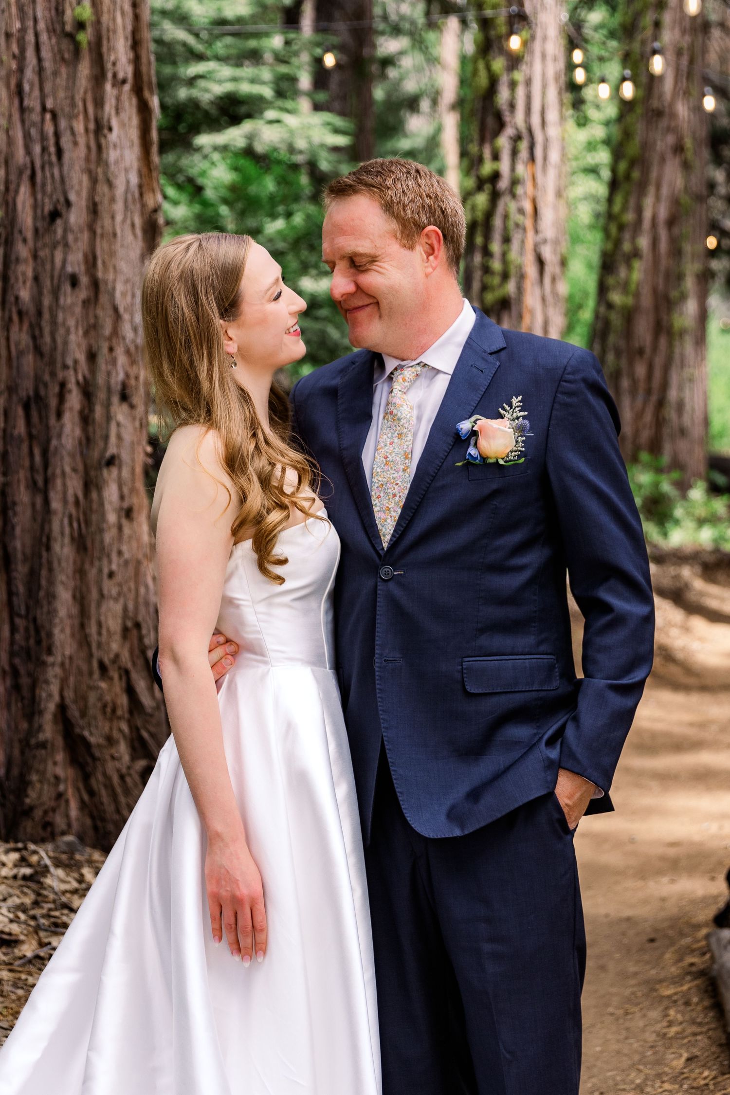 Couple in wedding attire sharing intimate moments among towering redwood trees.