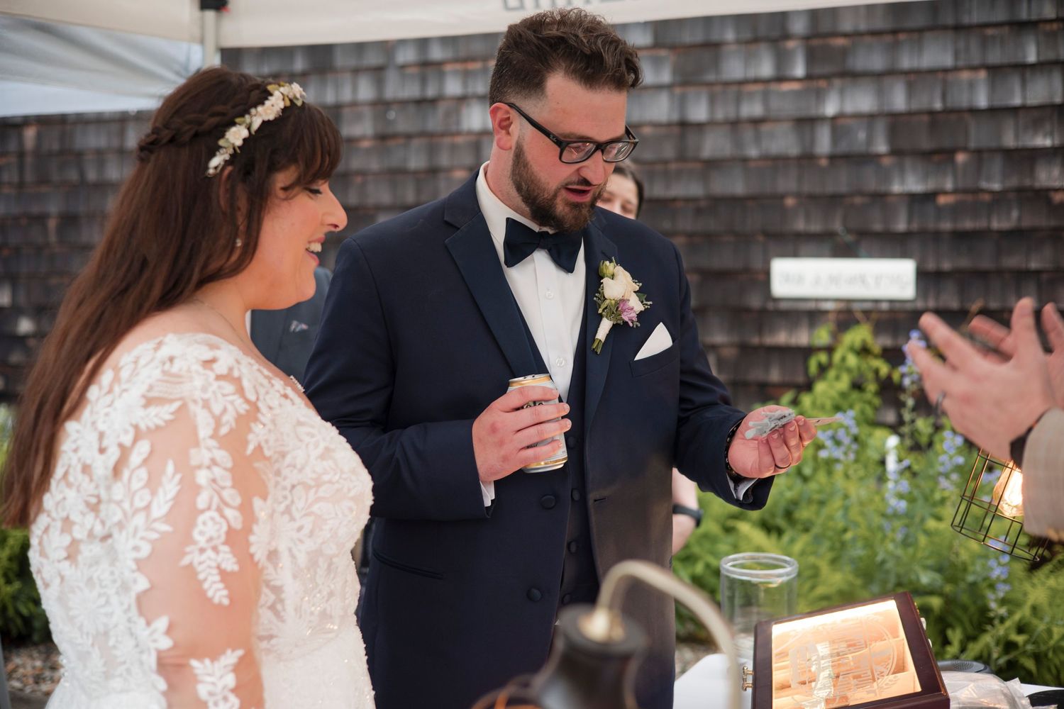 A couple shares a joyful moment during their wedding ceremony with lace dress and navy tuxedo details.