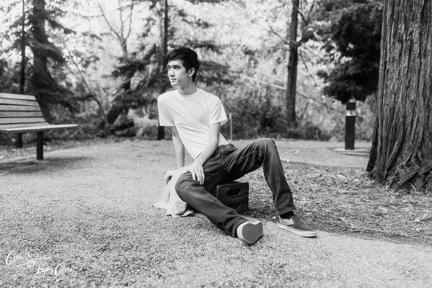 Person lounges casually outdoors against tall redwood trees in black and white scenic forest setting.