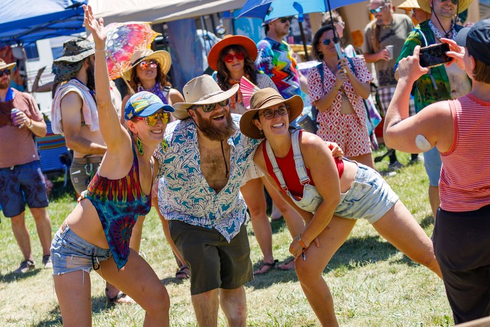 Festival goers dancing and posing outdoors at a sunny music festival wearing colorful summer outfits.