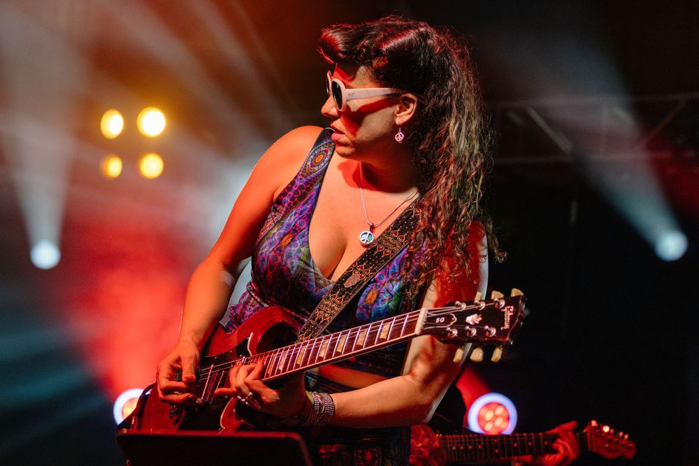 Musician playing electric guitar on stage with dramatic red and purple lighting effects.