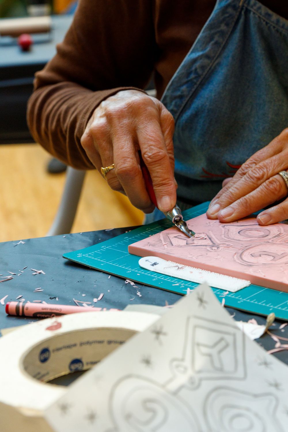 Artist carving intricate designs into a pink linoleum block using engraving tools on a cutting mat.