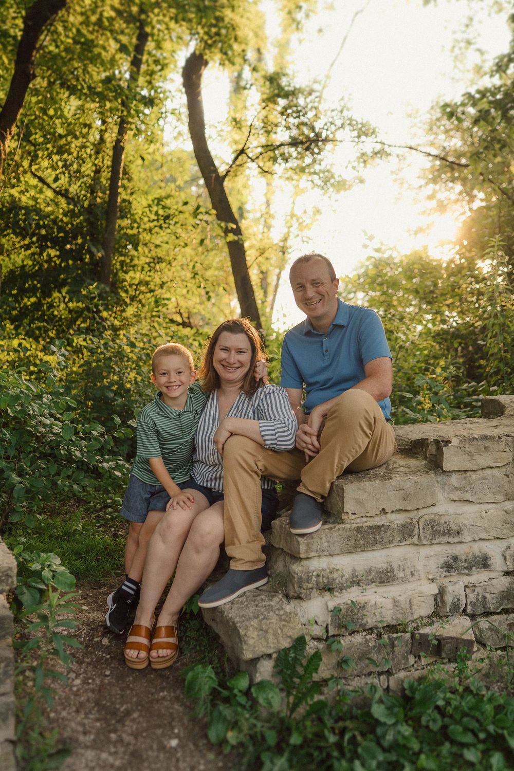 Family lounges casually together on old stone wall during golden hour photo session.