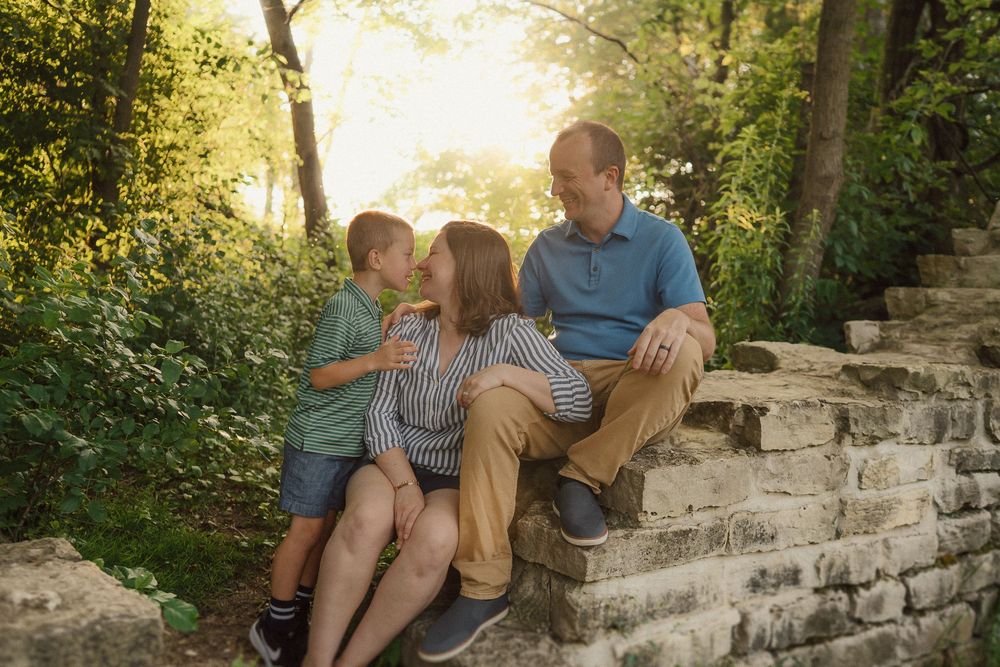 A family relaxes together on rustic stone steps surrounded by lush greenery and trees.