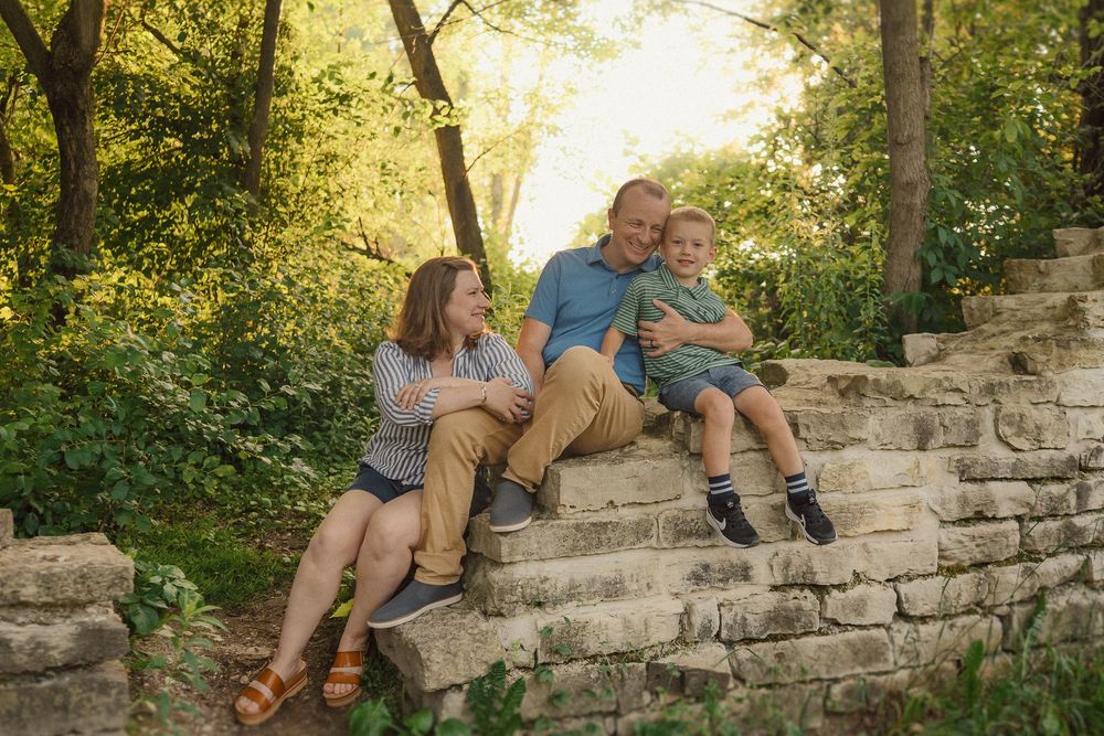 Family members sit casually on weathered stone steps in a natural outdoor setting at sunset.