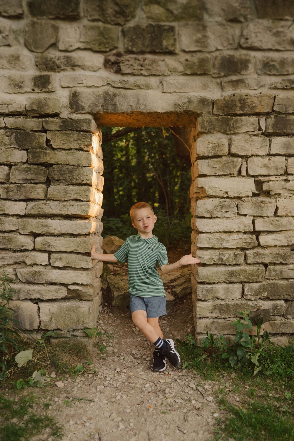 Child playfully poses through openings in old stone ruins during outdoor photography session.