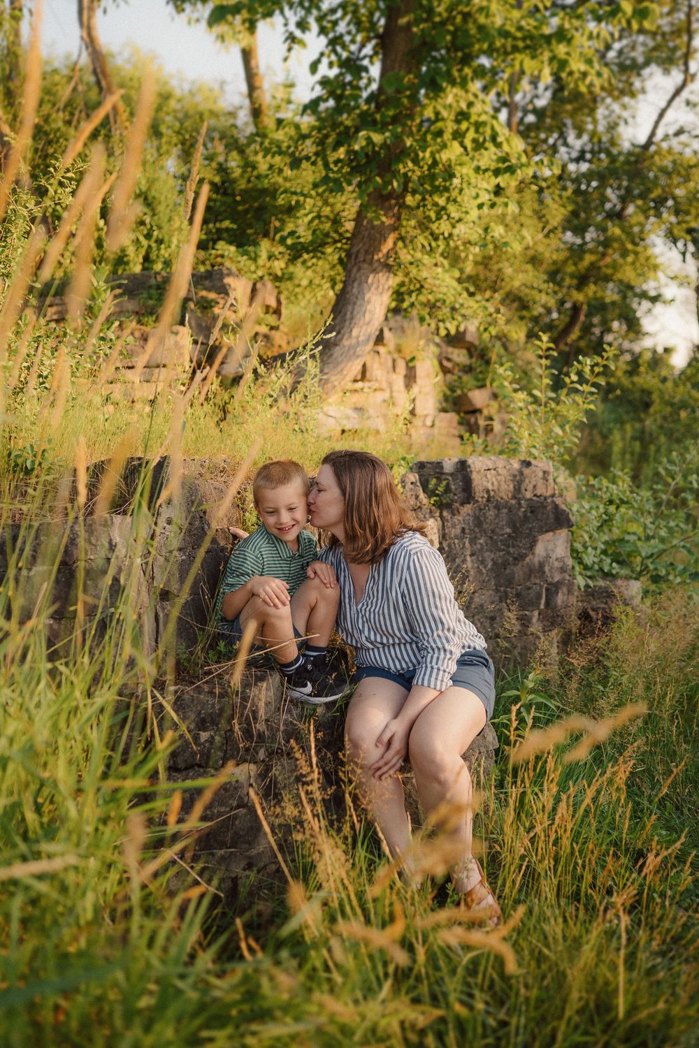 Family shares intimate moments together among tall grass and stone walls during golden hour.