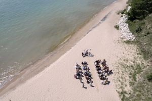 Aerial view of a group arranged in rows on a sandy beach next to turquoise waters.