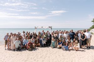 Large group gathered on a sunny beach shoreline with blue sky and water in the background.