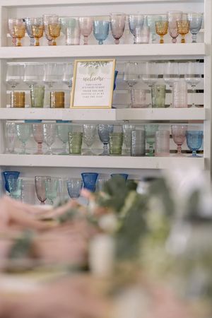 Vintage colored glass goblets and stemware displayed on white shelves with pastel pink, blue, and amber hues.