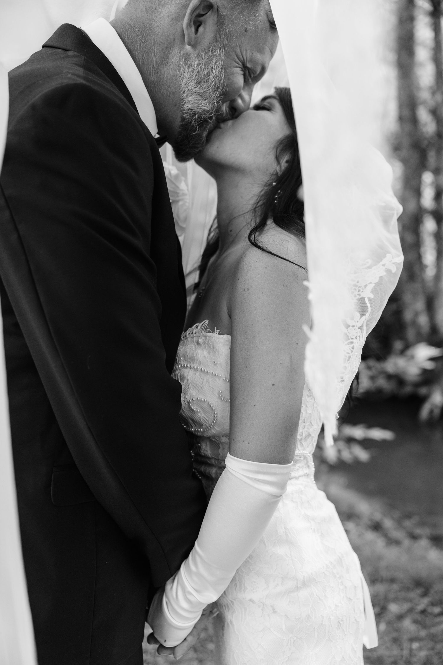 Black and white photo of a bride and groom sharing a kiss, bride wearing a veil and white gloves.