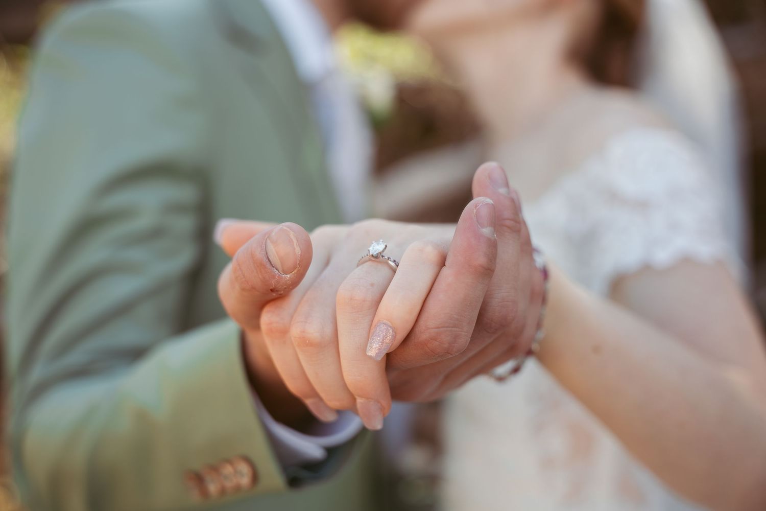 A couple stands in a sunlit meadow wearing wedding attire surrounded by evergreen trees during golden hour.