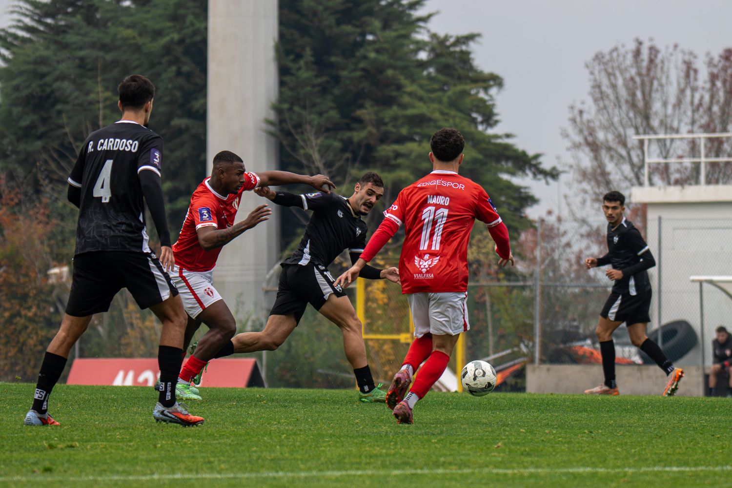 Soccer players in red and black jerseys compete for ball control during a match.
