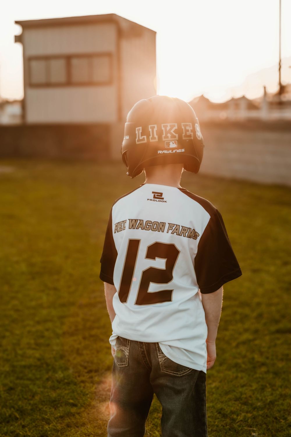 Baseball player wearing jersey number 12 stands on grassy field at sunset.