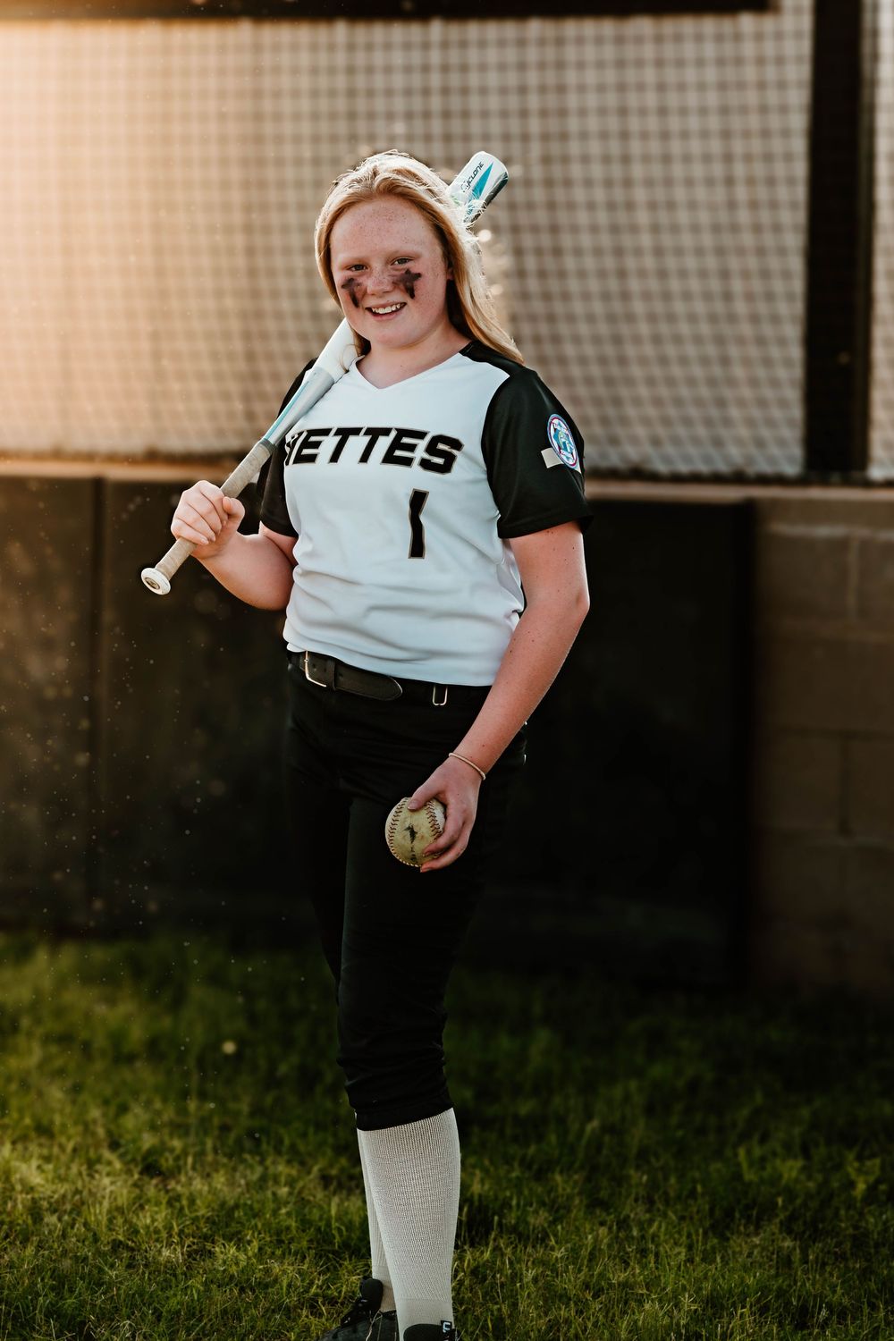 Young softball player in Nettes uniform practices on field at sunset.