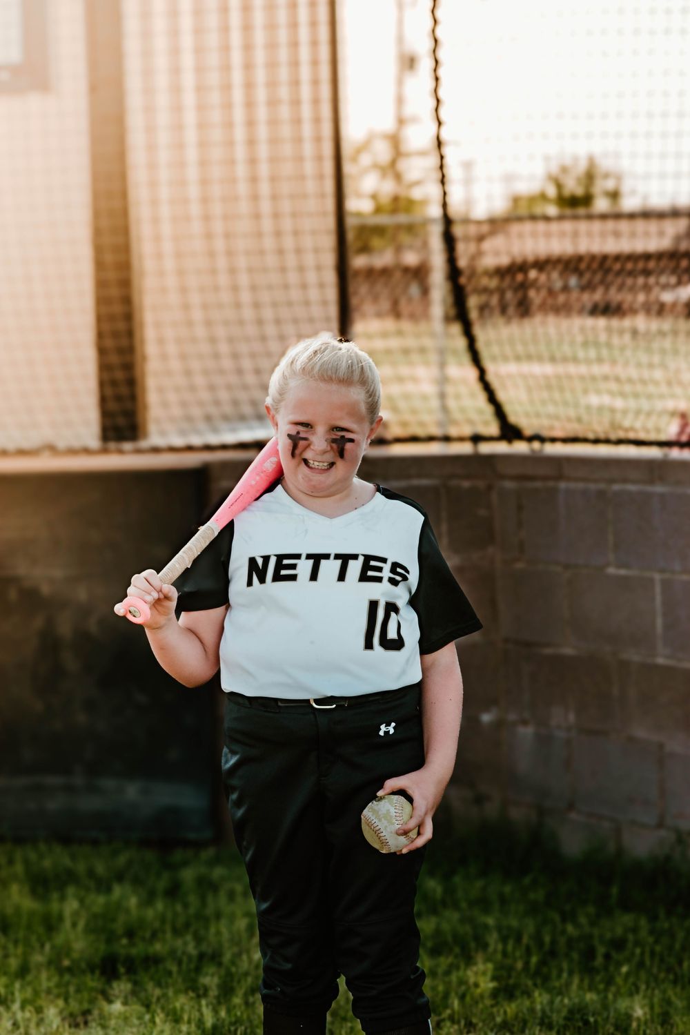 Young athlete in Nettes uniform holds softball equipment on field.