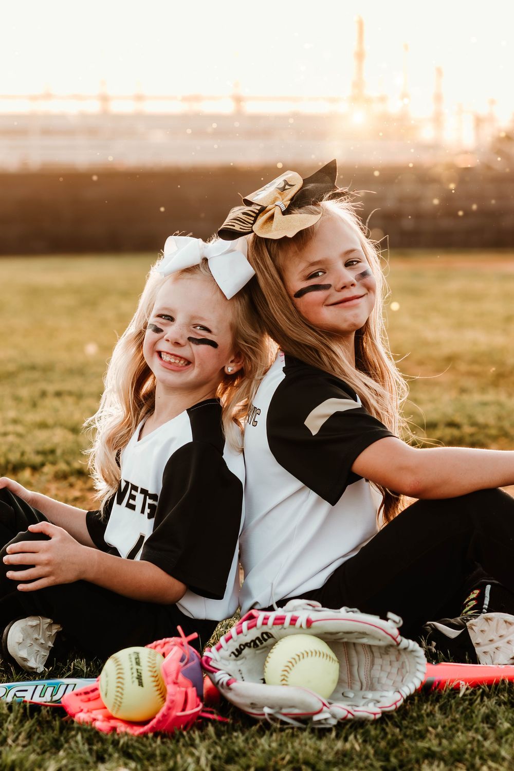 Softball players in uniforms lay on grass with softballs and equipment at sunset.