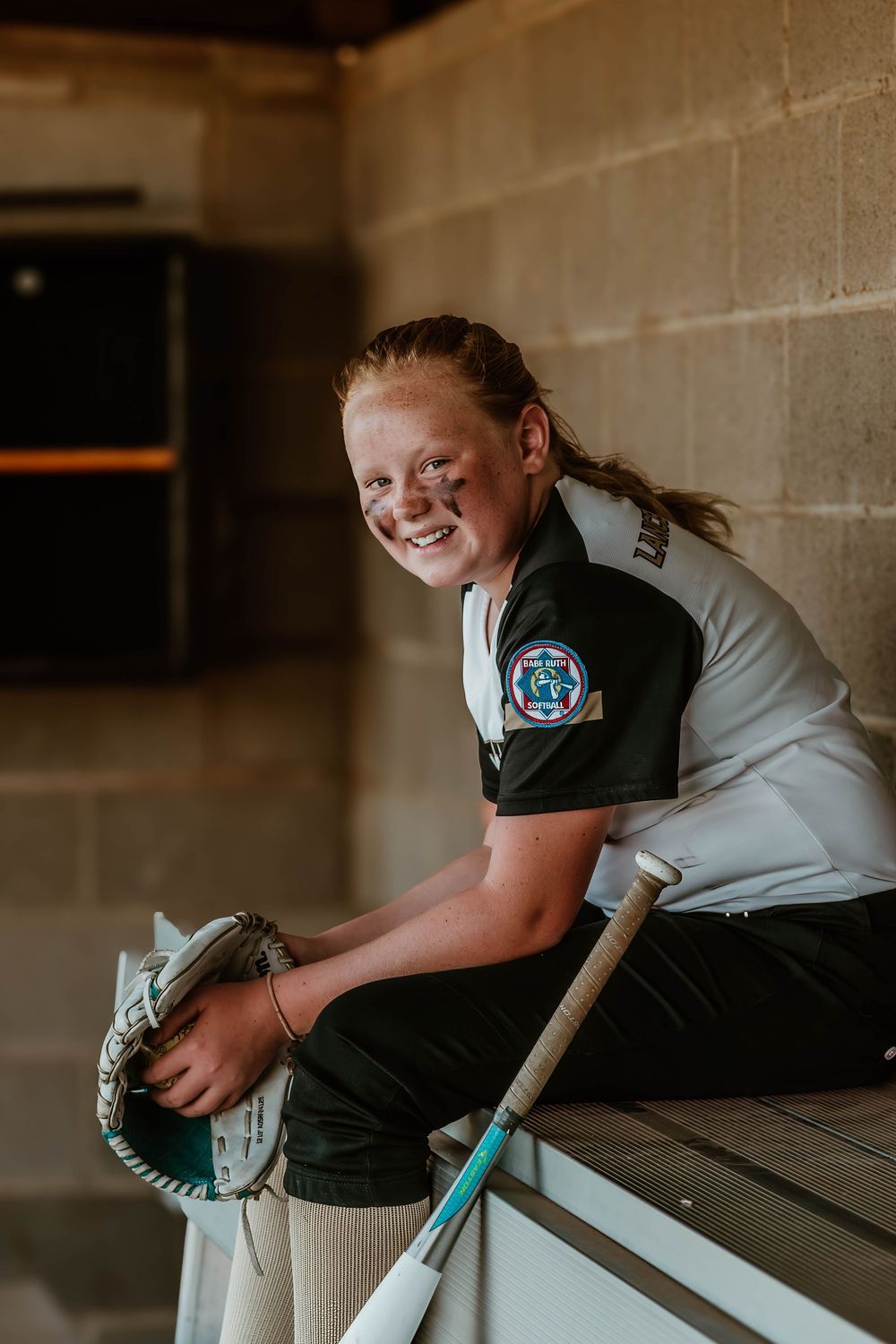 Young athlete in uniform practices softball techniques in dugout area.