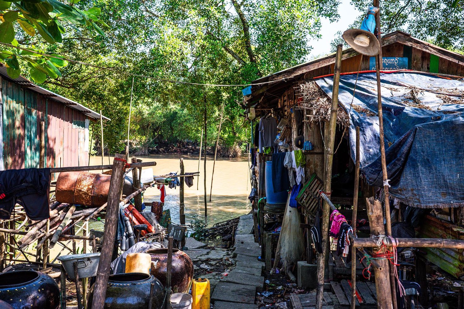 Outdoor marketplace with colorful tents and vendors selling goods under shady trees in a park-like setting.