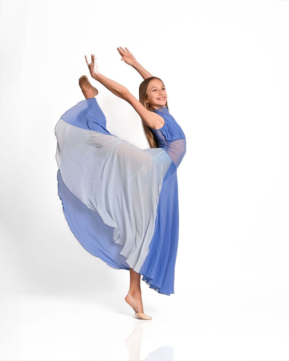A dancer in a flowing blue dress performs a graceful arabesque pose against a white background.