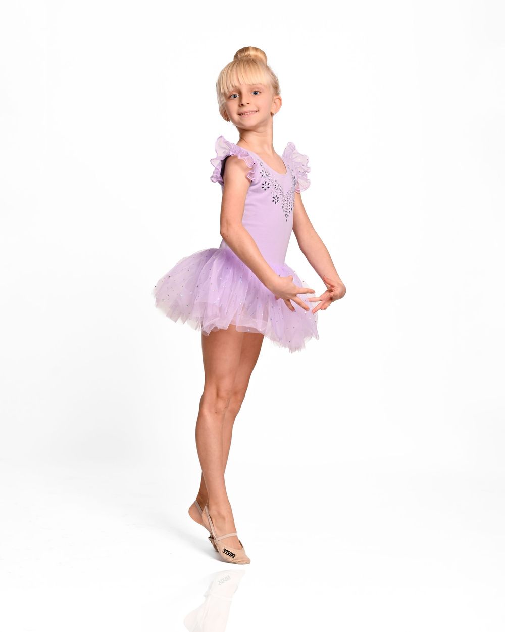 Young ballet dancer in lavender tutu performs graceful pose against white background.