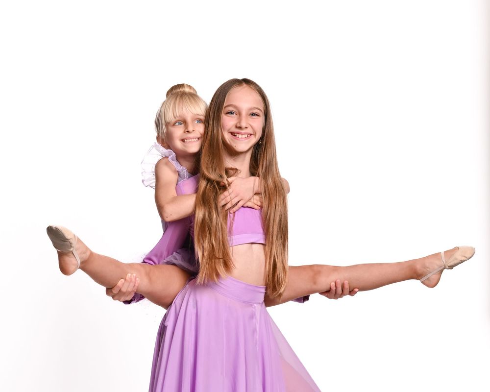 Young dancers in purple dresses strike graceful ballet poses against a white background.