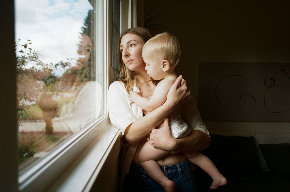 A parent and child sit together by a window in soft natural light, creating an intimate bonding moment.