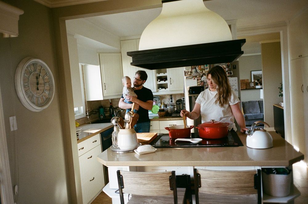Two people cooking together in a cozy kitchen with white cabinets and a wooden countertop under pendant lighting.