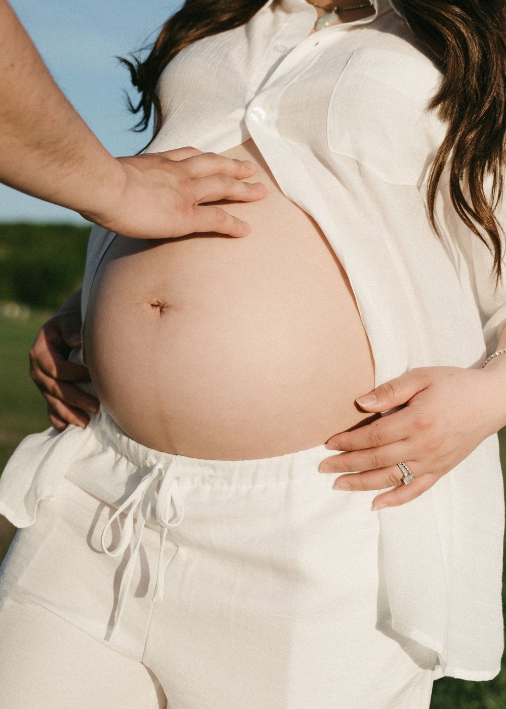 A series of photos showing a pregnant belly in a white dress with hands gently cradling the bump against a natural background.