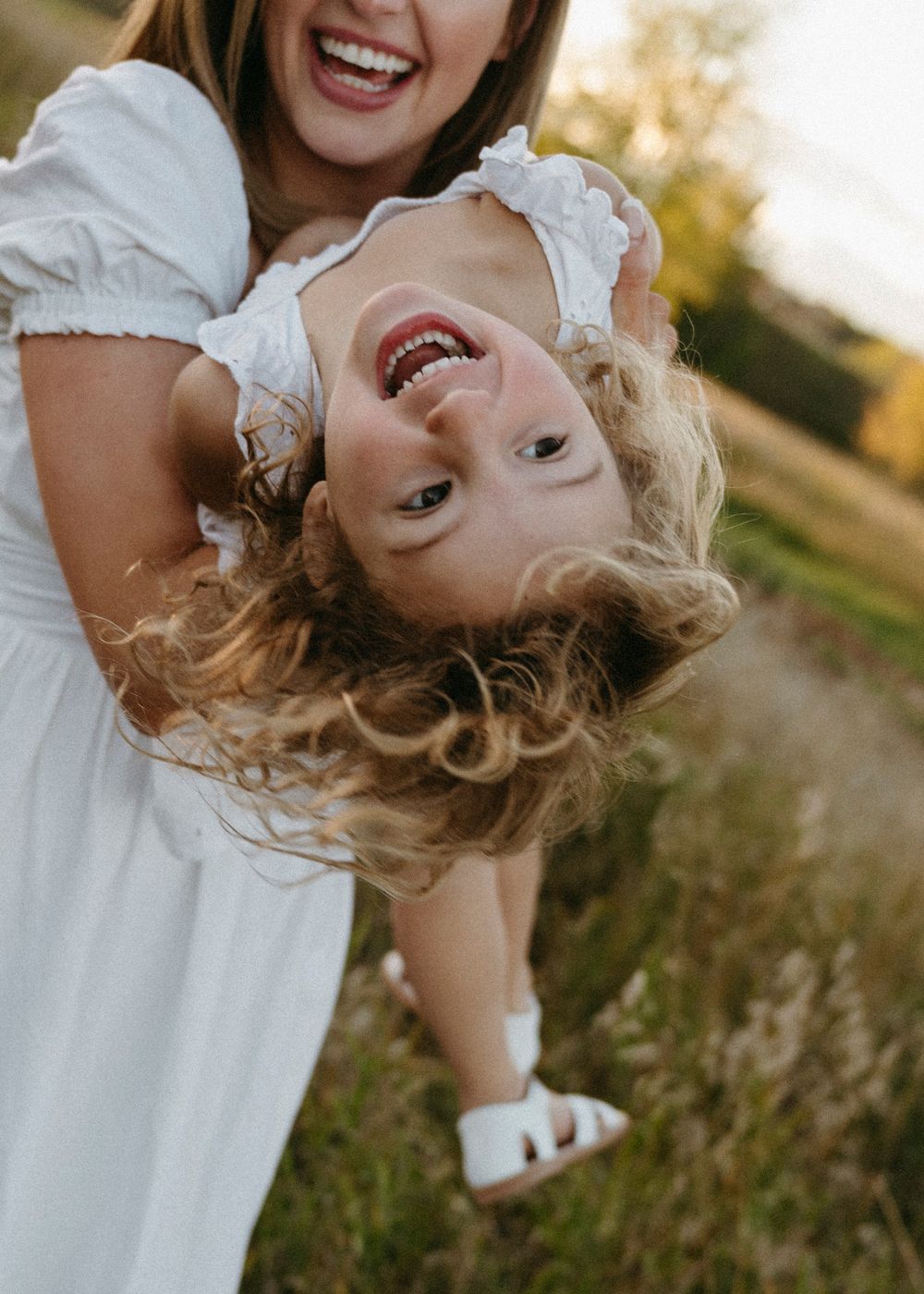 A person in a white dress spins and laughs joyfully in an outdoor setting during golden hour.