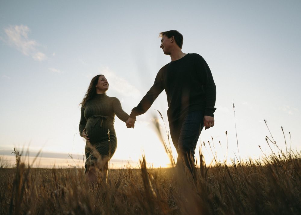 Silhouetted couple holding hands walks through tall grass field at sunset creating romantic outdoor scene.