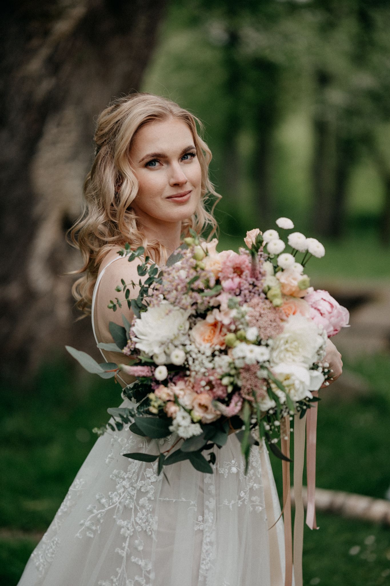 A romantic bridal portrait with a lush pink and white floral bouquet against a forest backdrop.