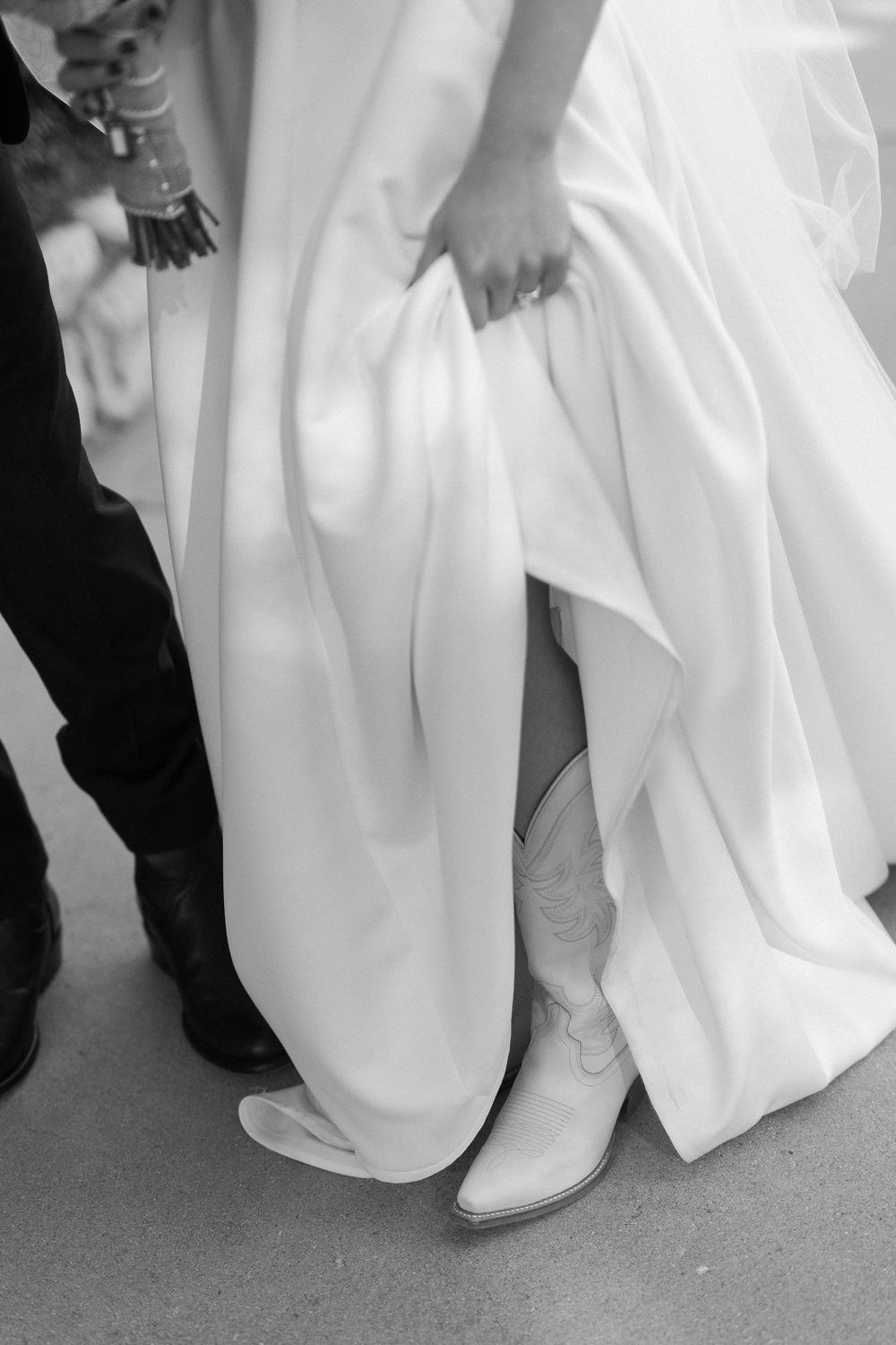 A black and white photo of a bride showing her cowboy boots underneath her wedding dress in Santa Barbara.