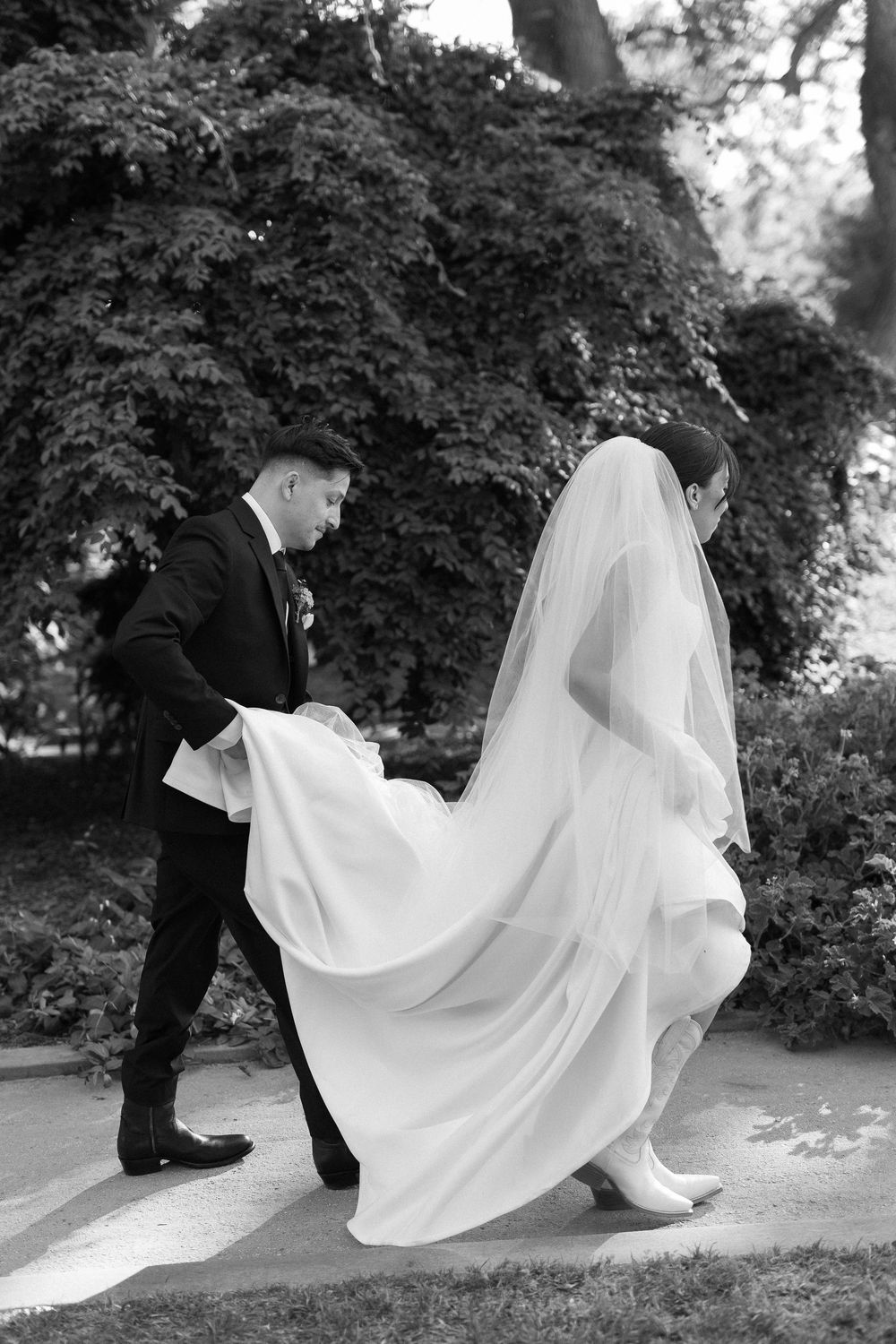 A black and white photo of a bride and groom walking through Alice Keck Memorial Gardens in Santa Barbara.