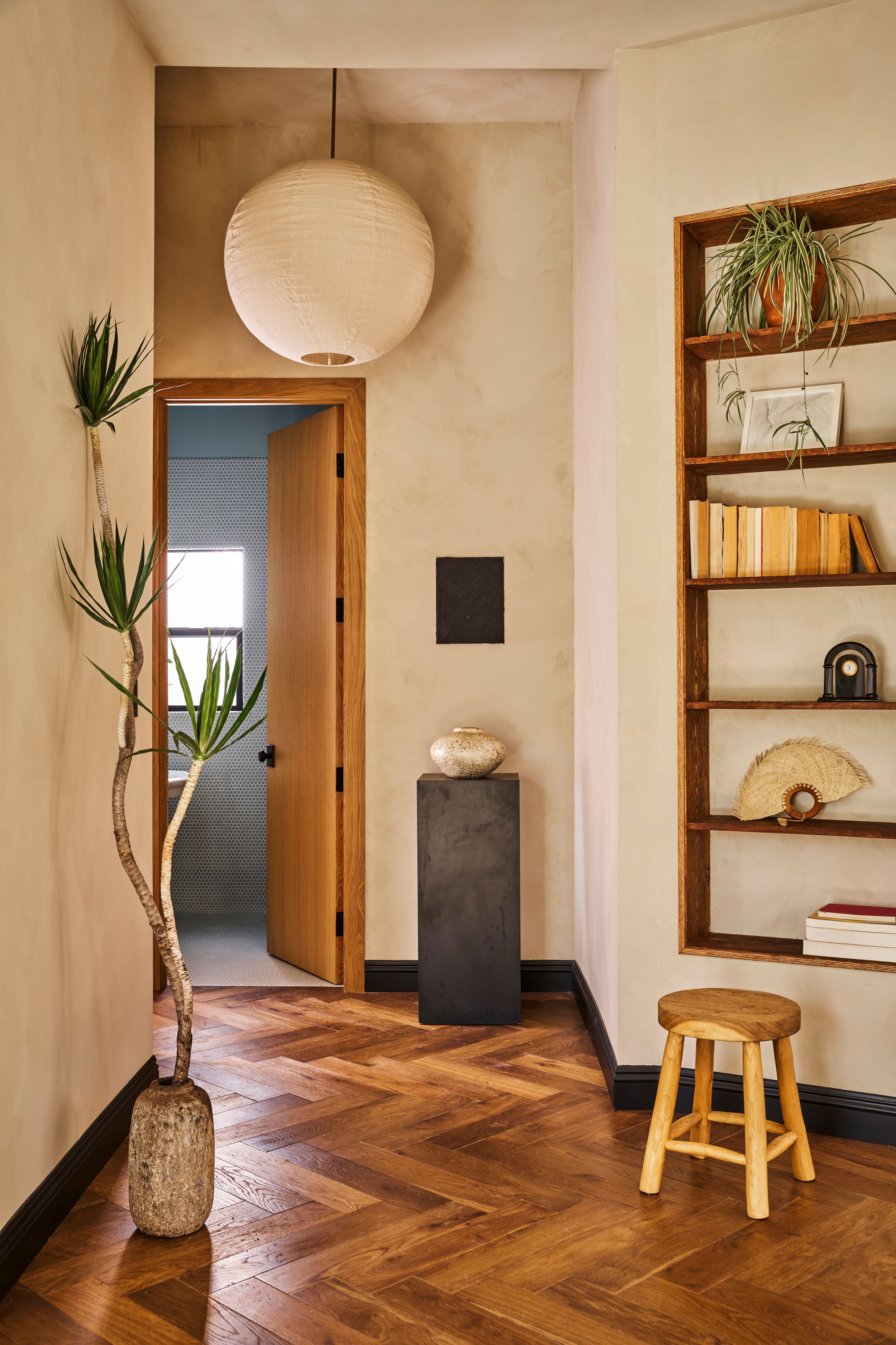 Modern minimalist interior with herringbone wood flooring, white walls, and decorative plants on floating shelves.