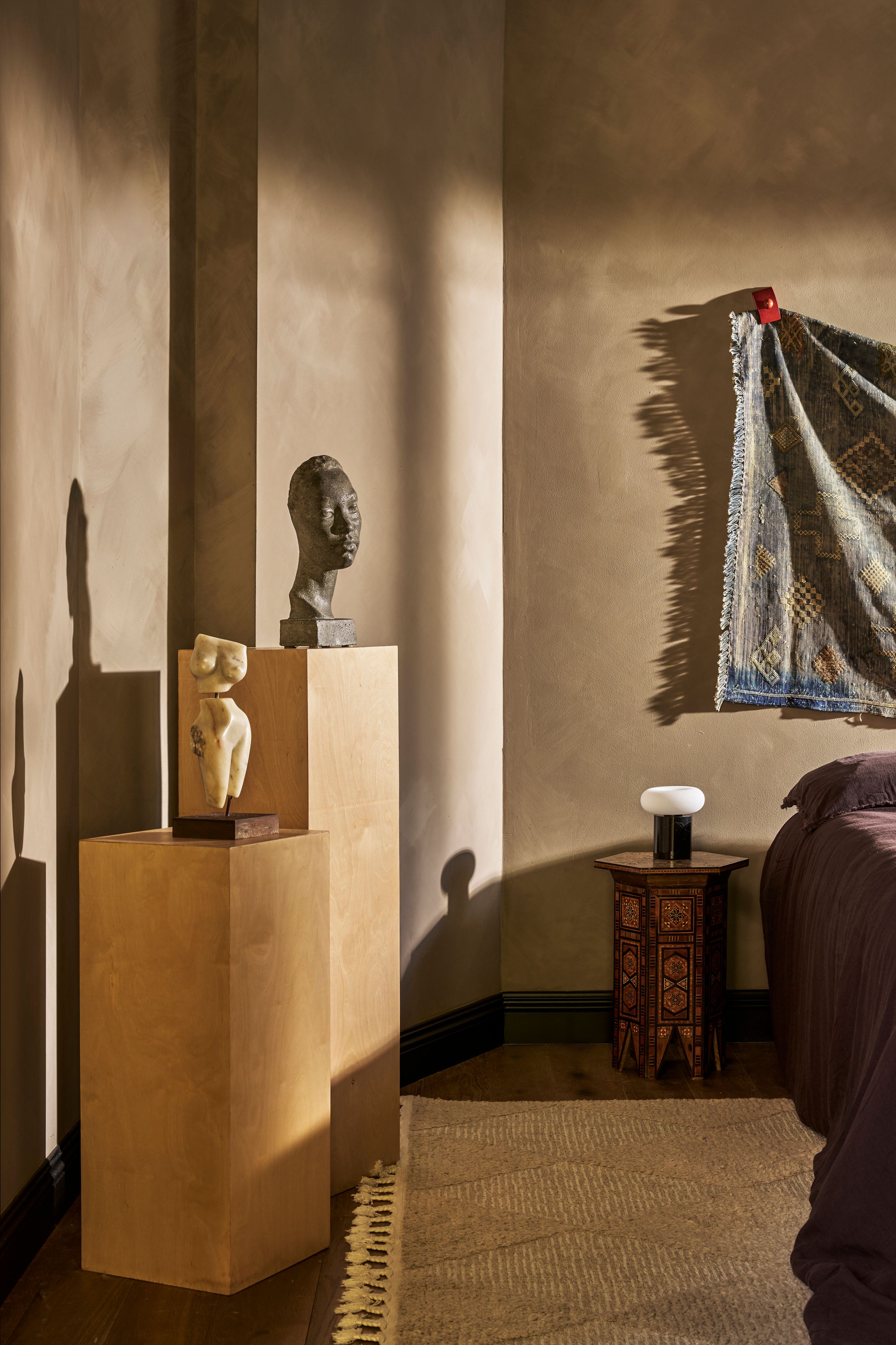 Interior corner with African art sculptures on wooden pedestals, tribal wall hanging, and side table in warm lighting.