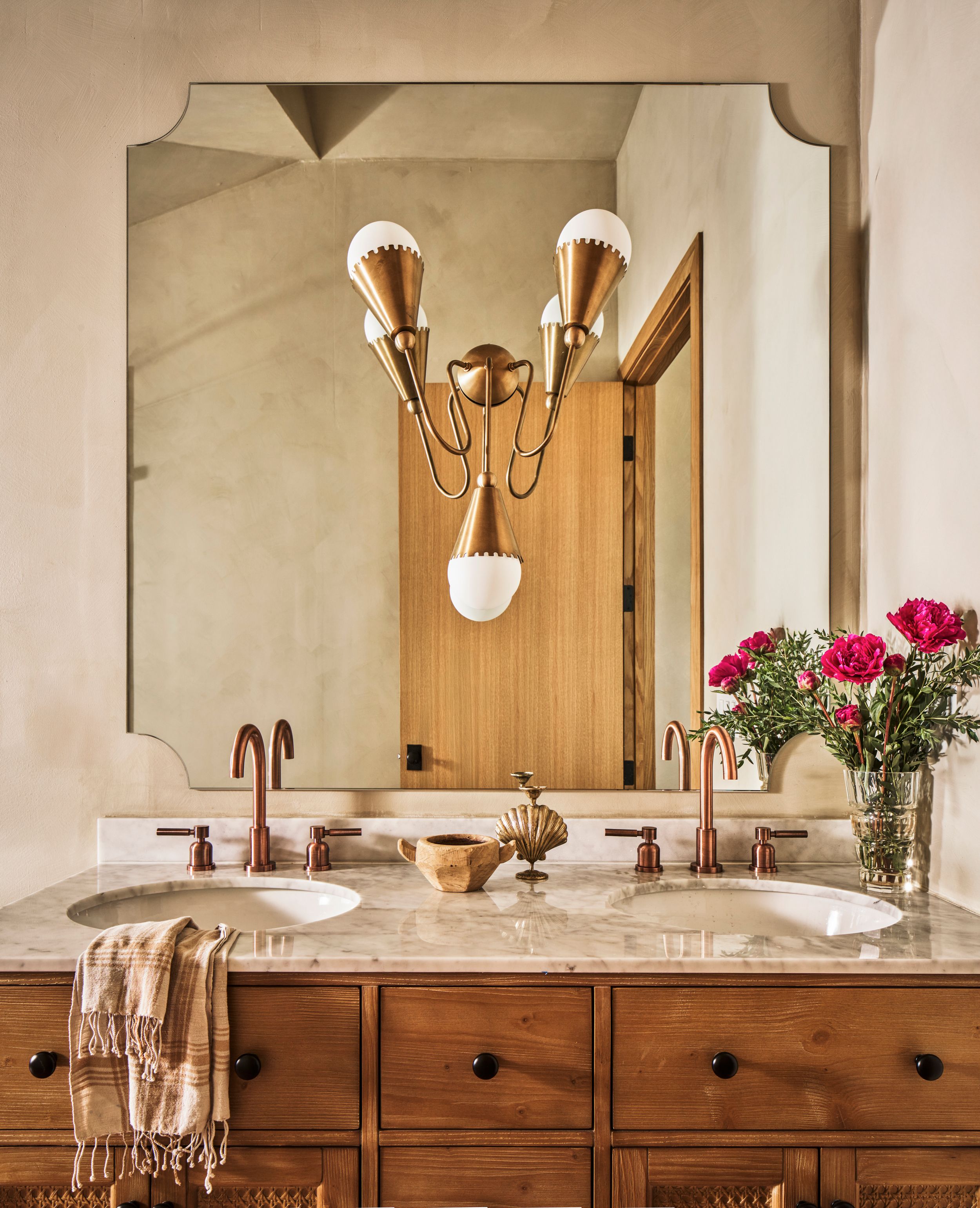 Elegant bathroom vanity with wooden cabinetry, marble countertop, and wall-mounted sconces creates a luxurious atmosphere.
