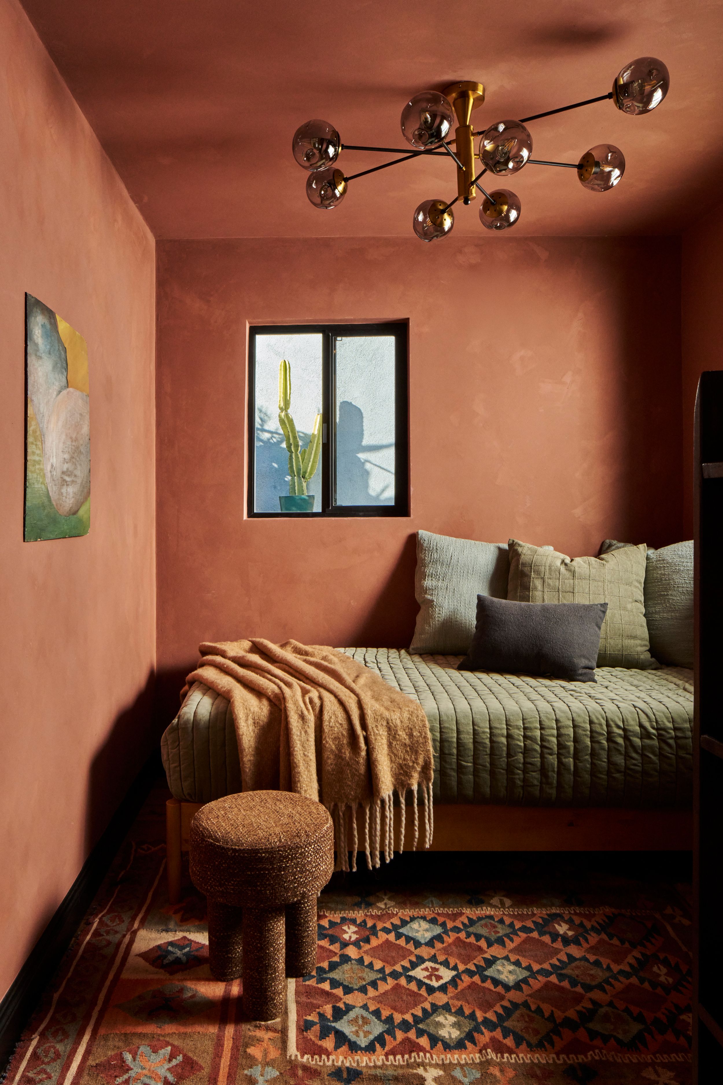 A cozy bedroom interior with terracotta walls, patterned rug, and green bedding showcases warm, earthy desert-inspired decor.