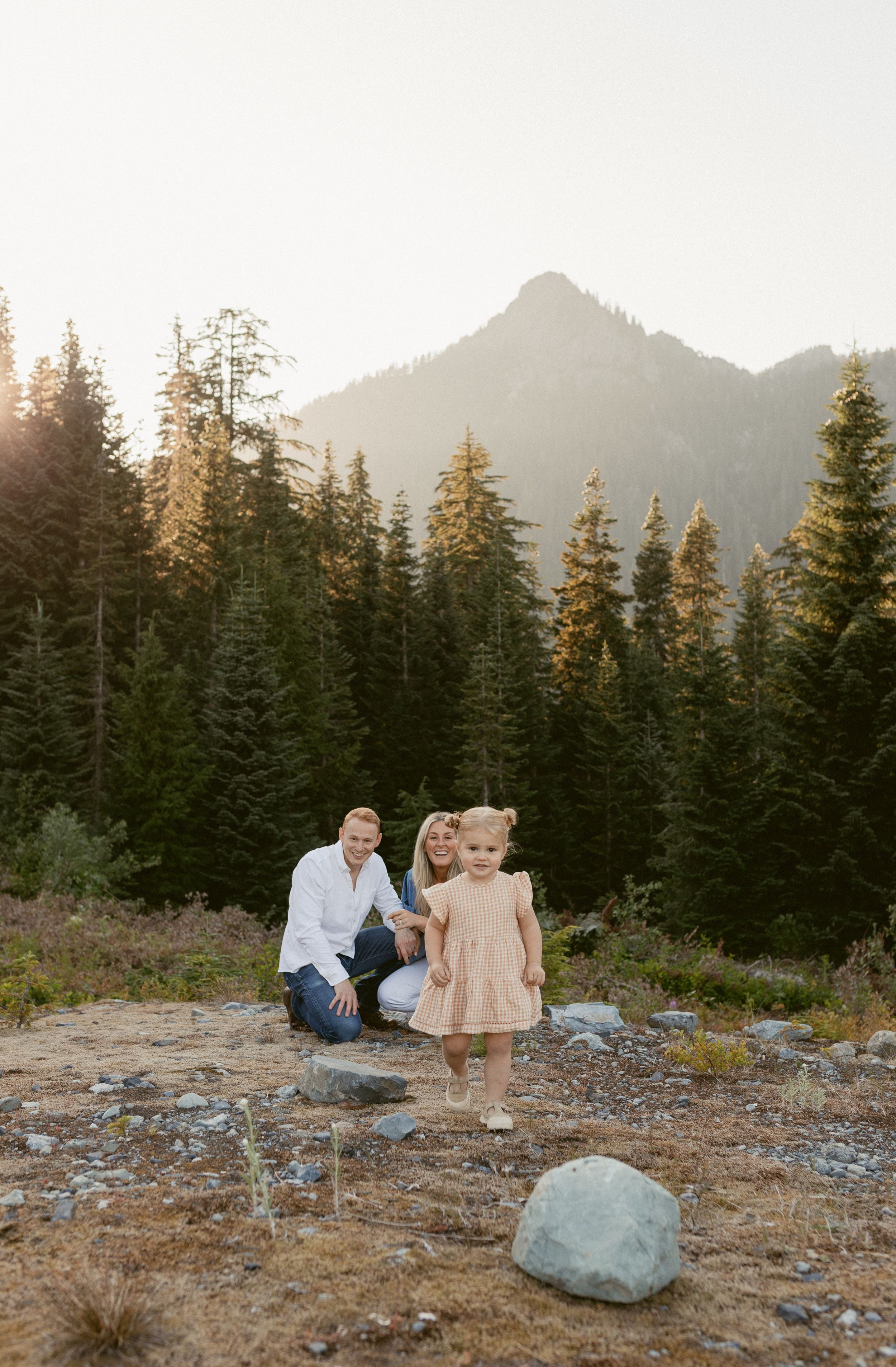 Family enjoying sunset together on rocky mountain terrain surrounded by evergreen trees.