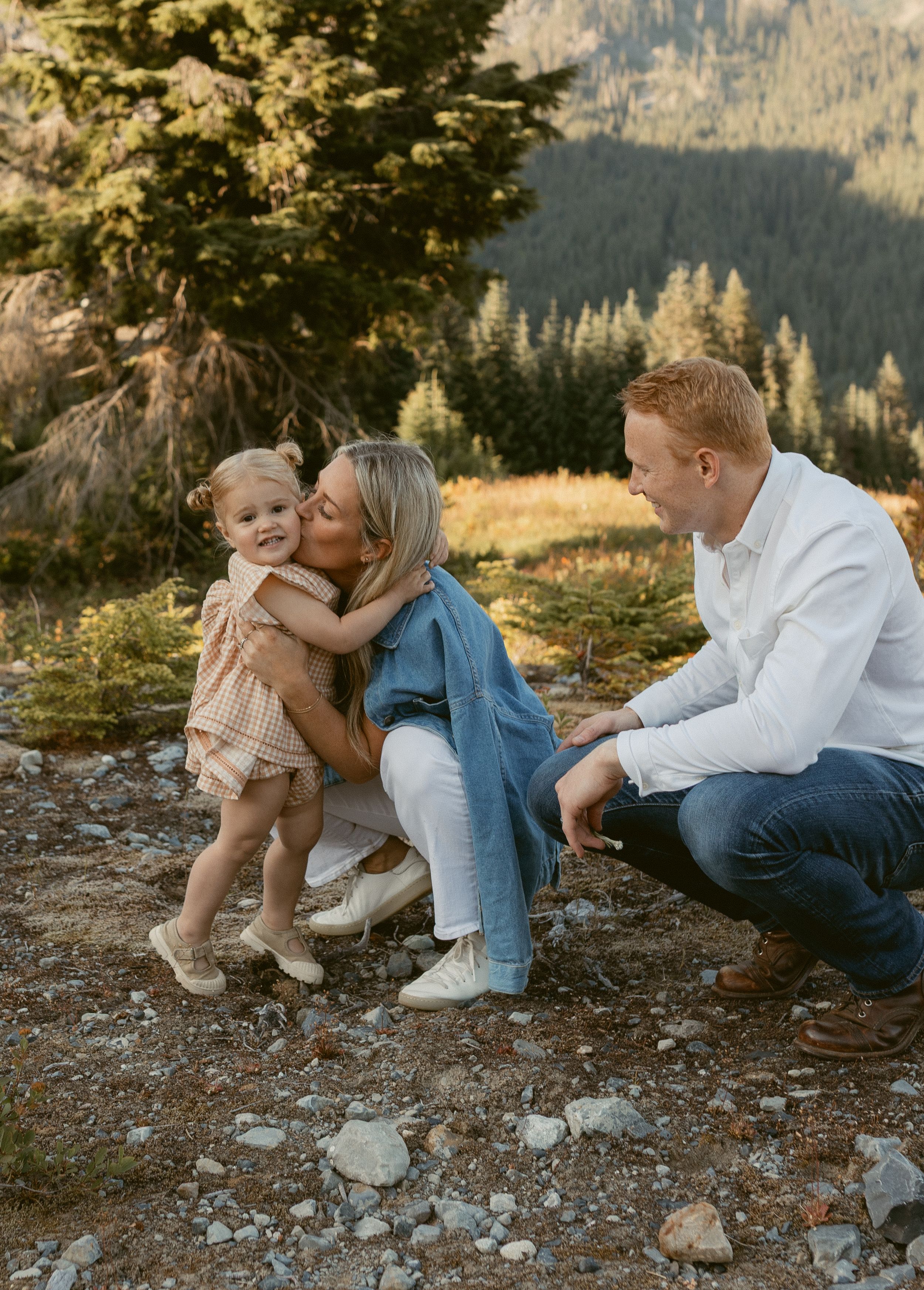 A family relaxes together on a rocky mountain slope during a golden hour outdoor photo session in nature.