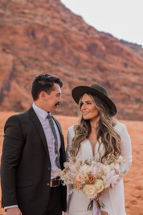 A couple shares romantic moments during their desert wedding photoshoot against stunning red rock formations.