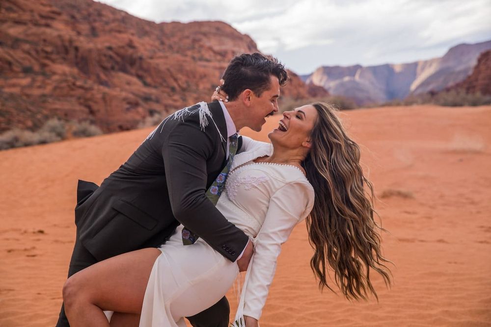 A romantic couple shares intimate moments while posing in the red sand desert landscape of Monument Valley.