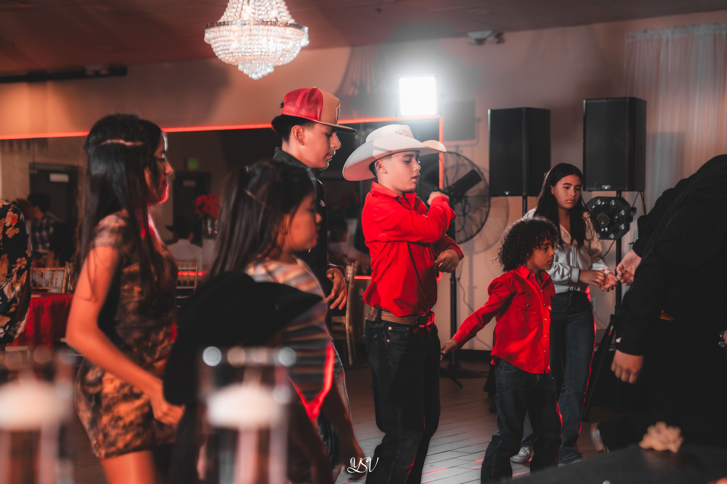 People dancing and socializing at a dimly lit nightclub or dance venue with red lighting accents.