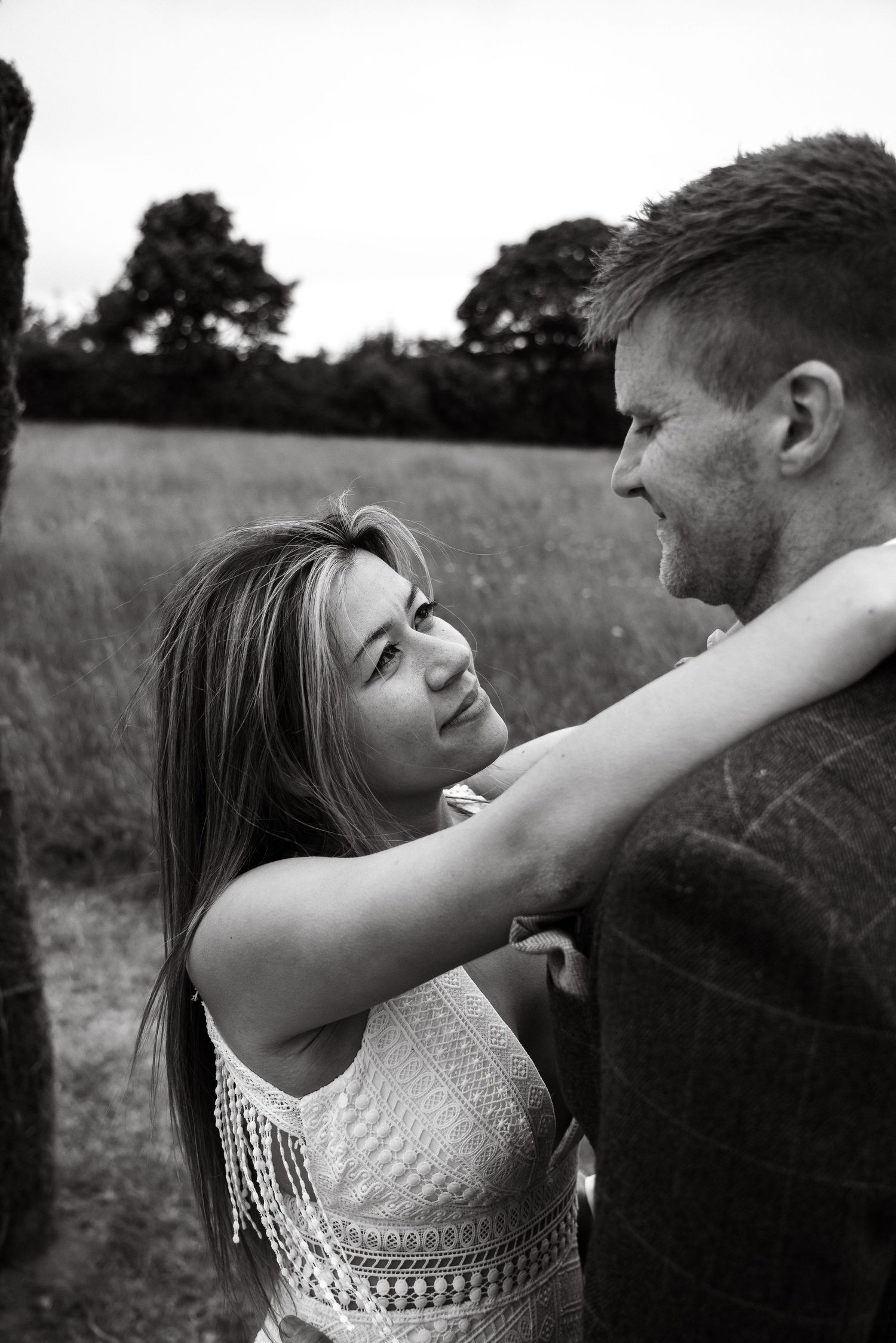 Black and white portrait of a couple sharing an intimate moment in a field.