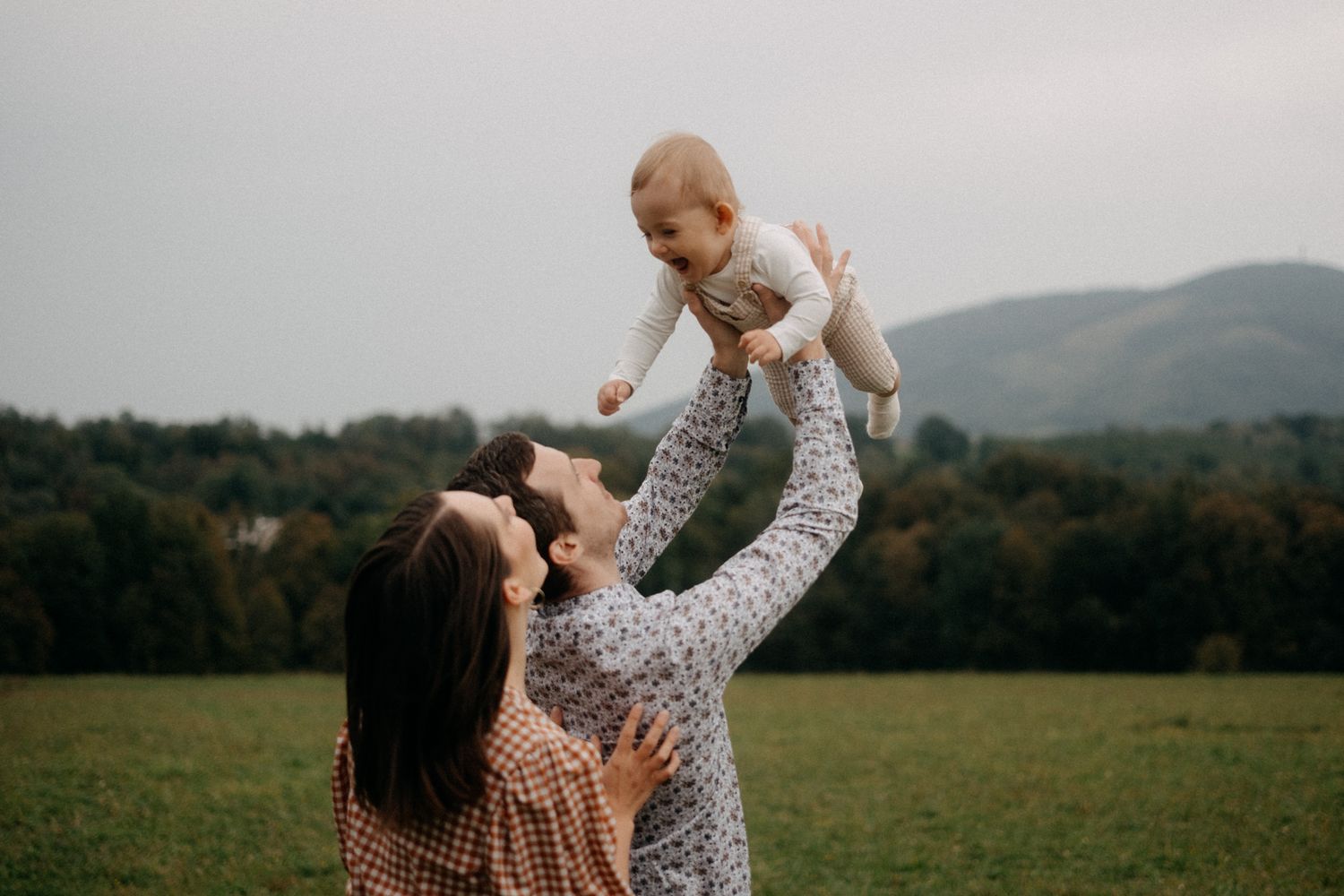 Parent and child share playful moments on a blanket in a mountain field.