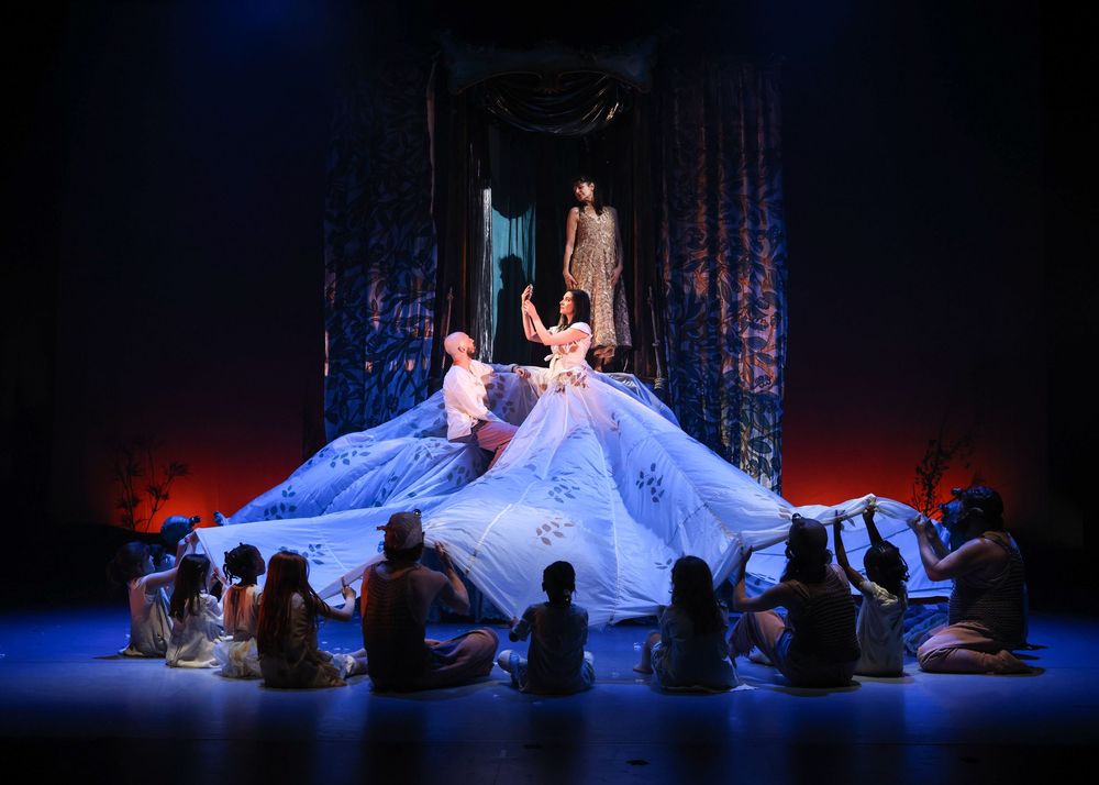 Ballet dancers in white costumes perform on a dimly lit stage with ethereal blue lighting effects.