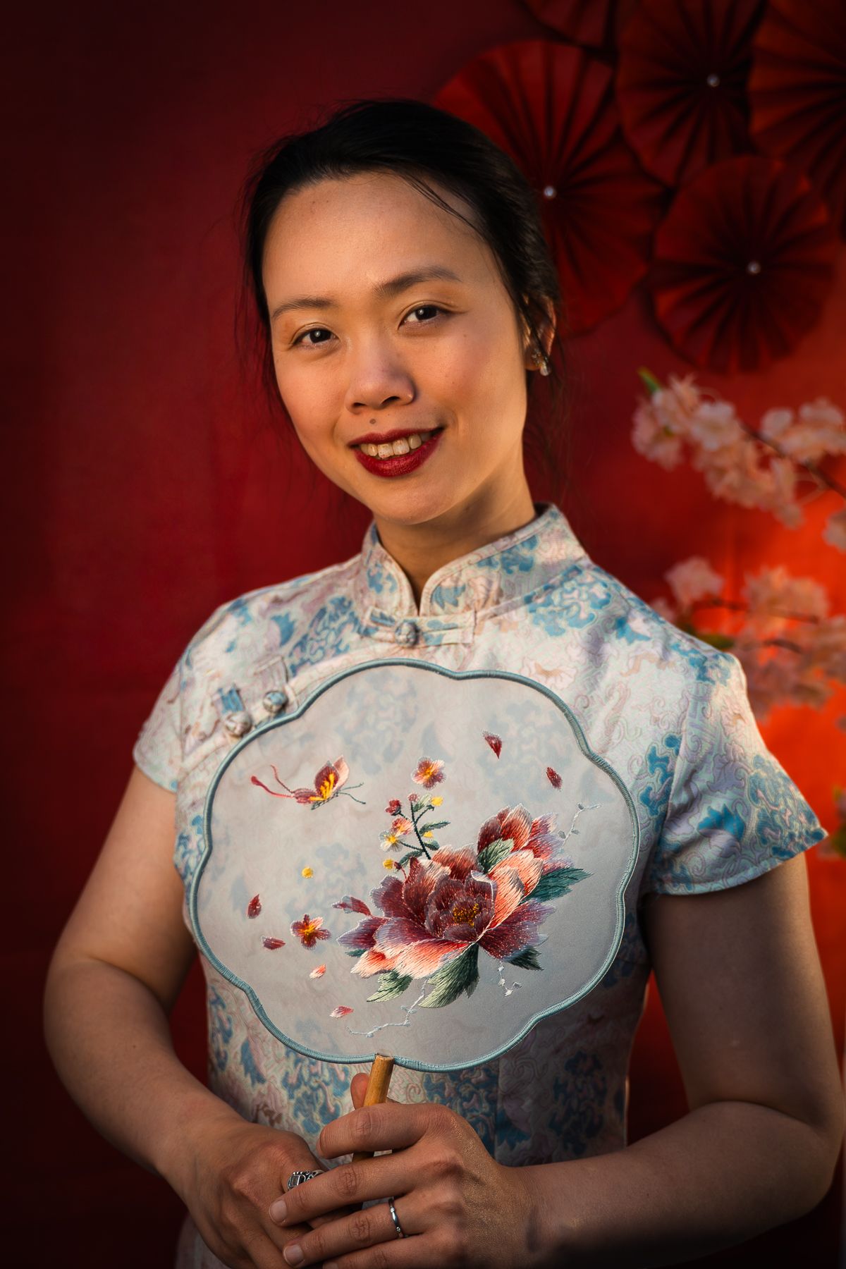 A portrait of a lady traditional Chinese qipao dress against a red backdrop with decorative props by Melbourne Chinese New Year Photographer