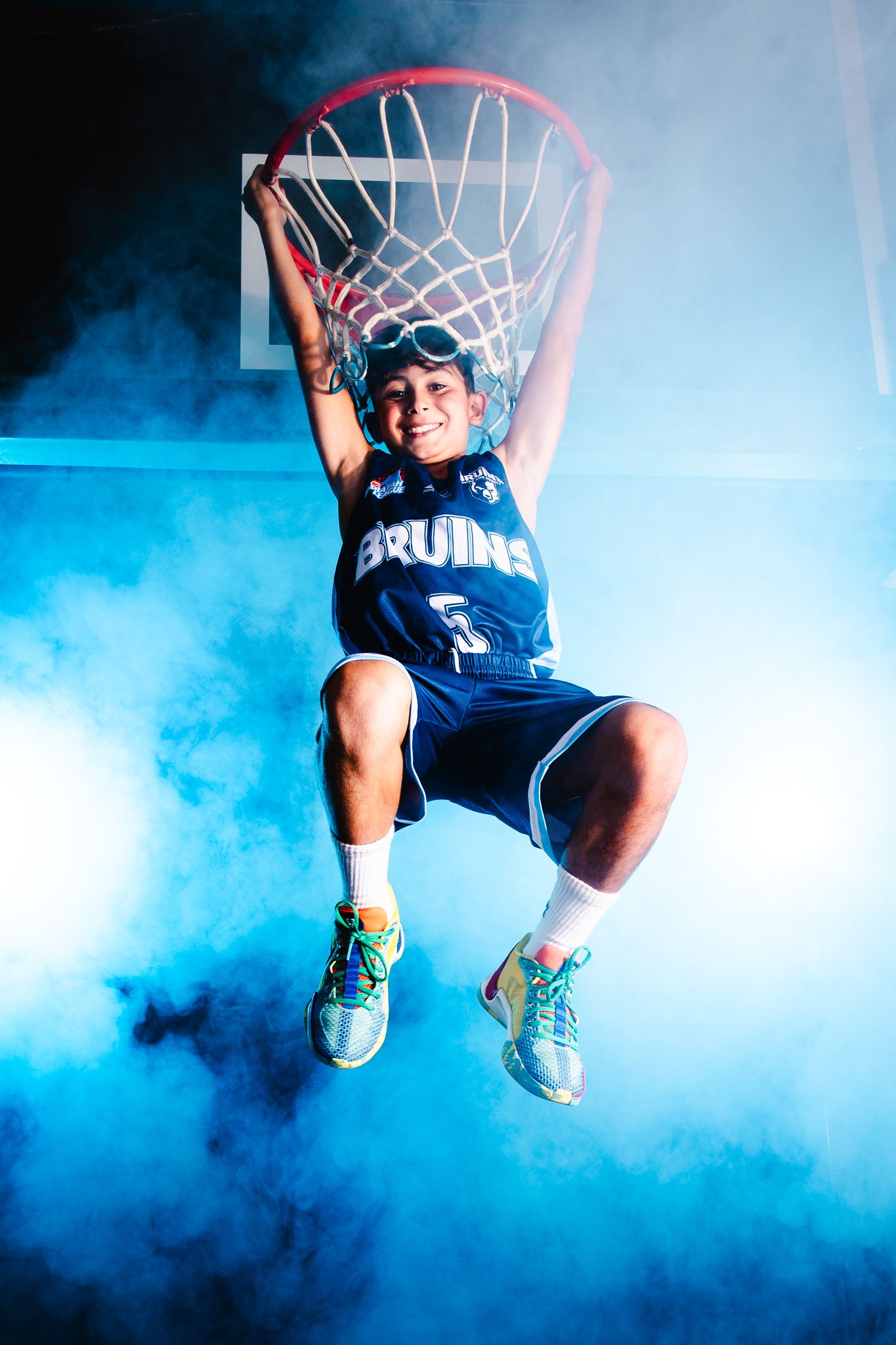 Basketball player in blue Bruins jersey hangs from hoop with dramatic blue smoke effects.