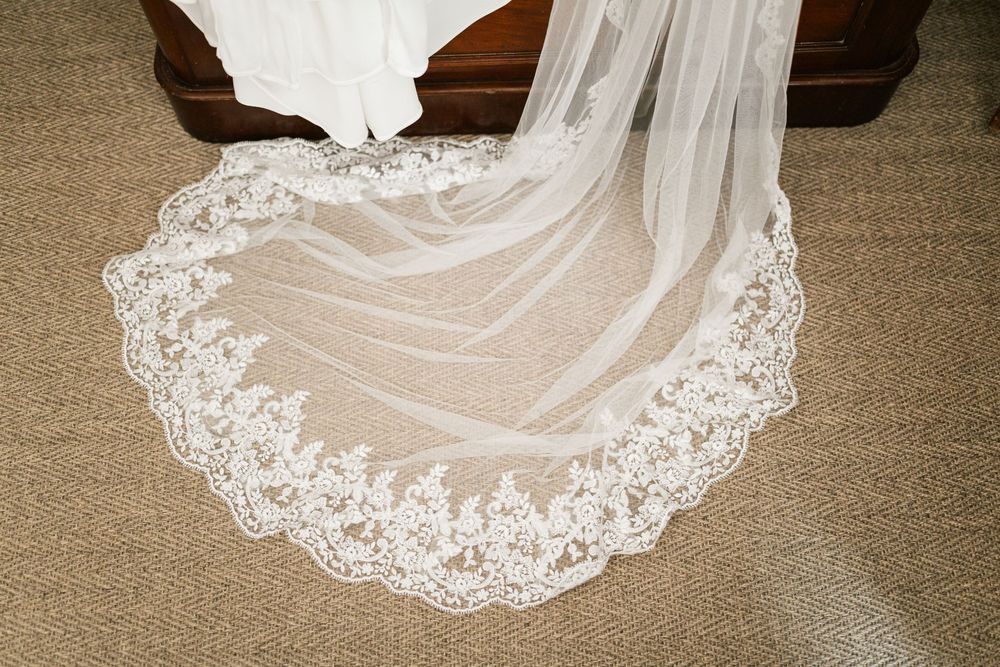 Elegant white wedding dress with intricate lace detailing laid out on a beige carpet showing the flowing hemline.