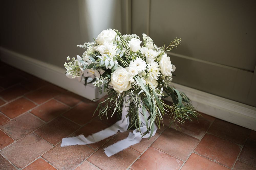 A romantic white and green wedding bouquet with roses and greenery rests on terracotta tiles.